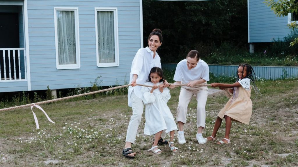 A happy family enjoys a game of tug of war in a grassy field by a house.