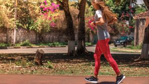 A woman jogs on a path surrounded by trees and vibrant flowers, embodying a healthy lifestyle.